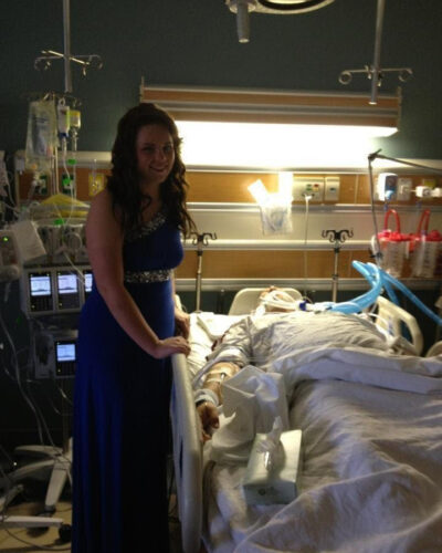 Woman standing by hospital bed, patient lying down.
